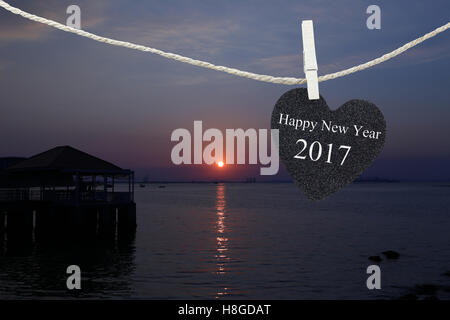 Cuore nero appeso sulla corda di canapa su sfondo di sunrise e sono felice anno nuovo 2017 testo. Foto Stock