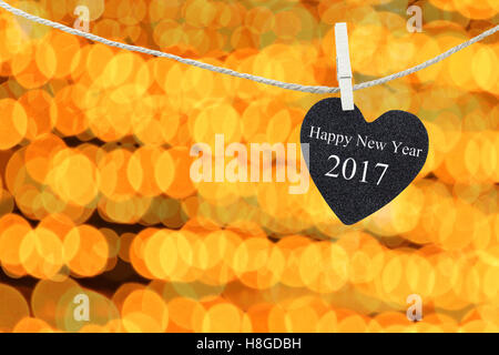 Cuore nero appeso sulla corda di canapa sul bokeh di fondo di un colore dorato e di sfondo sono di colore bianco di felice anno nuovo 2017 testo. Foto Stock