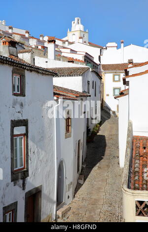 MARVAO, PORTOGALLO: una tipica strada di ciottoli con le sue case dipinte di bianco e tetti di tegole con la Torre dell Orologio in background Foto Stock