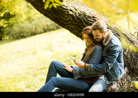 Felice l'uomo e la donna utilizza lo smartphone in autunno park Foto Stock