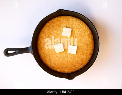 Il burro sulla fusione cornbread calda che era cucinato in una ghisa nera skillett isolato su bianco Foto Stock