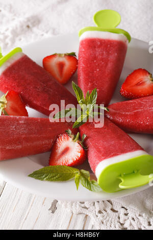 Gustosa fragola ghiaccioli su un bastone su una piastra di close-up verticale. Foto Stock