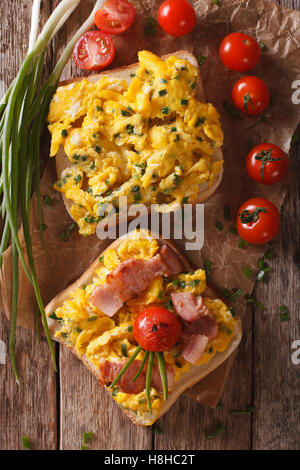 Sandwich fatti in casa con uova strapazzate, pancetta e pomodori vicino sul tavolo. vista verticale da sopra Foto Stock