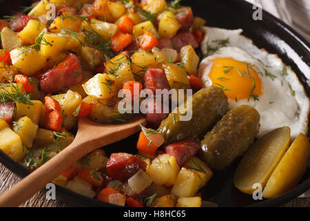 Prima colazione scandinava: pyttipanna con uova fritte e cetrioli sottaceto close-up su una piastra orizzontale. Foto Stock