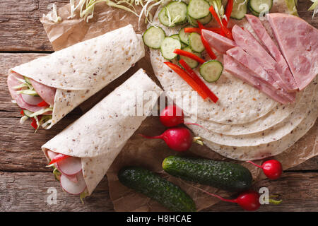 Rulli a sandwich con prosciutto e formaggio e verdure fresche di close-up e gli ingredienti sul tavolo. vista orizzontale dal di sopra Foto Stock