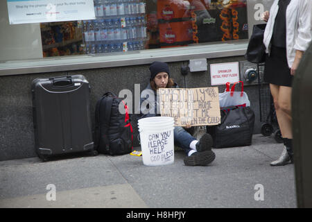 Senzatetto uomo seduto sul marciapiede di raggiungere fuori per aiutare lungo la settima Avenue nel centro di Manhattan. Foto Stock