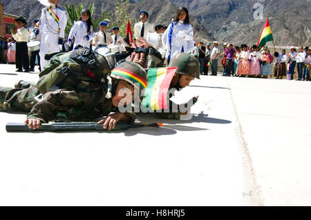 Sfilata in Bolivia rurale con abiti fantasiosi bambini soldato strisciando sul terreno. Ragazzo che guarda in telecamera, Foto Stock