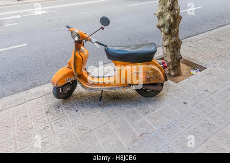 Un vecchio nero e arancione Super Vespa scooter è parcheggiato su un marciapiede in Barcellona, Spagna. Foto Stock