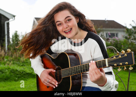 Ragazza adolescente tenendo una chitarra acustica al di fuori mentre sorridente verso la telecamera Foto Stock