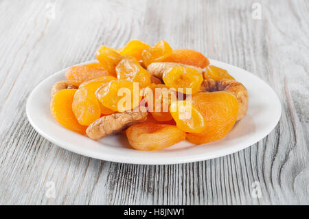 Frutta secca su un sfondo di legno. Frutta candita, limone, albicocca, figg. Frutti nella piastra bianca. Foto Stock