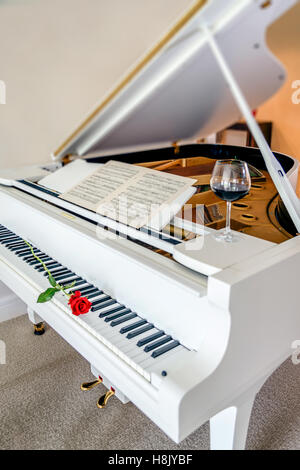 Una rosa rossa sul pianoforte con foglio di musica e un bicchiere di vino rosso Foto Stock