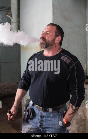 Uomo Barbuto fuma sigaretta elettronica. Foto Stock