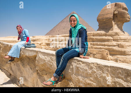 Cairo, Egitto due le donne egiziane di sedersi di fronte alla Grande Sfinge di Giza con le Piramidi di Giza in background. Questo Foto Stock
