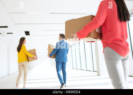 Vista posteriore di imprenditrice con colleghi che trasportano le scatole di cartone a muoversi in ufficio vuoto Foto Stock