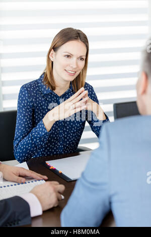 Fiducioso giovane imprenditrice discutendo con colleghi di sesso maschile in sala riunioni Foto Stock
