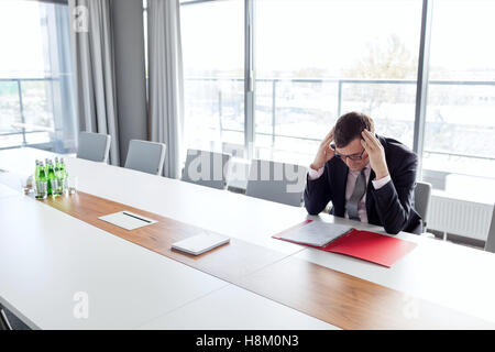 Imprenditore maturo che soffrono di mal di testa al tavolo nella sala riunioni Foto Stock