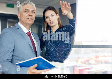 Giovane imprenditrice mostrando qualcosa di maturare imprenditore visto attraverso il vetro Foto Stock