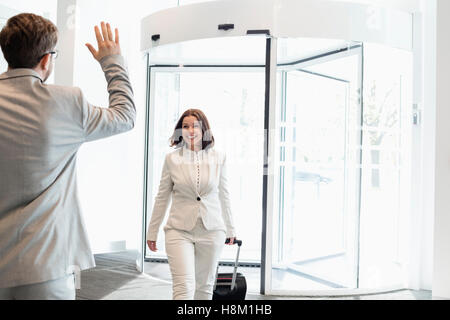 Felice imprenditrice con bagagli camminando verso il collega di sesso maschile in convention center Foto Stock