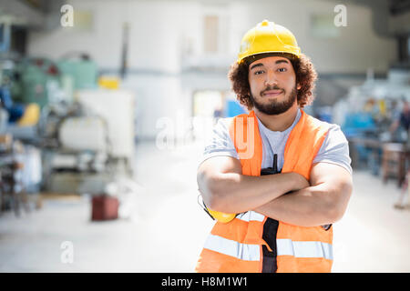 Ritratto di giovane lavoratore manuale in piedi con le braccia incrociate nella industria del metallo Foto Stock