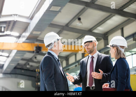 La gente di affari che indossa hardhats avendo discussioni nell industria del metallo Foto Stock