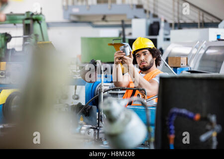 Giovane lavoratore manuale esaminando il metallo in fabbrica Foto Stock