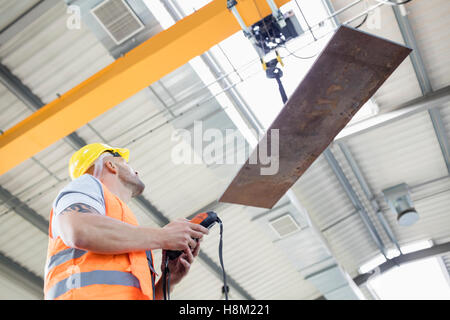 Basso angolo vista del lavoratore manuale operativo sollevamento gru lamiera nell'industria Foto Stock