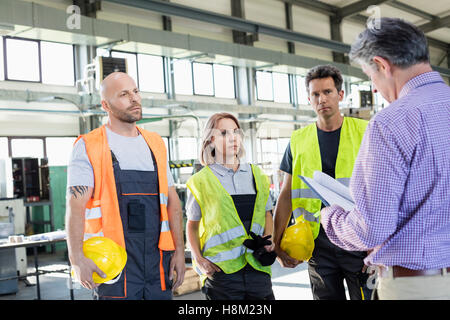 Ispettore maschio esaminando il file da lavoratori manuali dell'industria Foto Stock