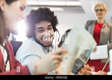 Sorridente giovane imprenditore che indossa la cuffia con i colleghi in ufficio Foto Stock