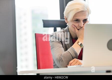 Grave imprenditrice maturo utilizzando laptop alla scrivania in ufficio Foto Stock