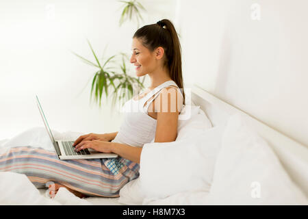 Donna sorridente recuperando i social media come lei si rilassa in letto con un computer portatile su un giorno pigro Foto Stock