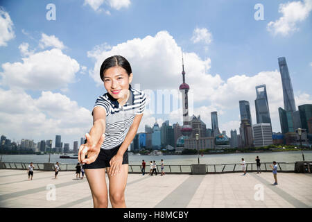 Ritratto di donna felice gesti segno di pace mentre si sta in piedi sul lungomare contro lo skyline di Pudong Foto Stock