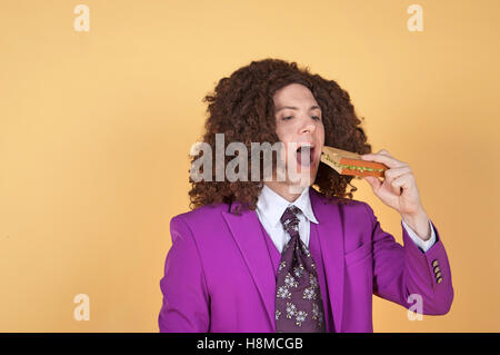 Uomo caucasico con Afro indossa vestito viola mangiare panino Foto Stock