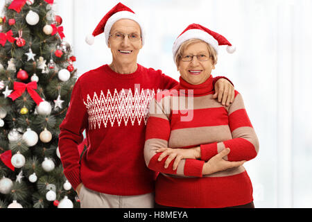 Allegro coppia senior con cappelli di Babbo Natale nella parte anteriore di un albero di Natale Foto Stock