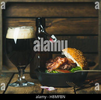 Hamburger di manzo con pancetta croccante e un bicchiere di birra scura Foto Stock