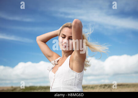 Donna bionda in piedi in campo con le mani nei capelli Foto Stock