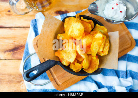 Patate fritte in padella con la salsa di aglio e una birra su di un tavolo di legno Foto Stock