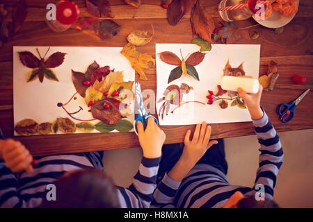 Dolce bambino, ragazzo, applicando le foglie utilizzando colla pur facendo arti e mestieri di scuola, tempo di autunno Foto Stock