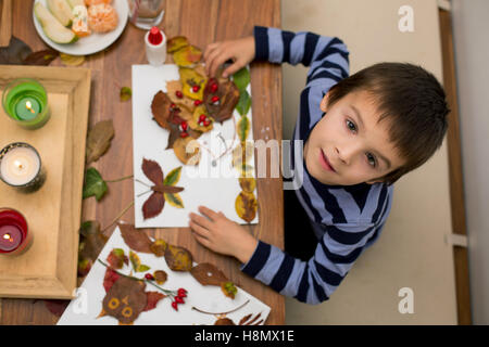 Dolce bambino, ragazzo, applicando le foglie utilizzando colla pur facendo arti e mestieri di scuola, tempo di autunno Foto Stock