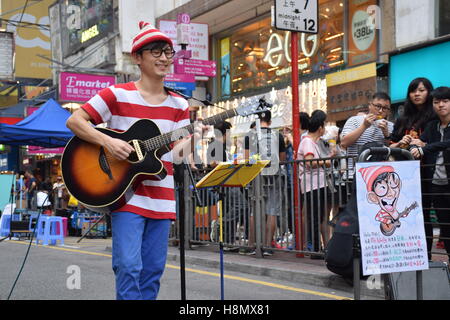 Hong kong cina - il giovane ragazzo asiatico a suonare la chitarra e cantare sulla strada con la sua caricatura Foto Stock