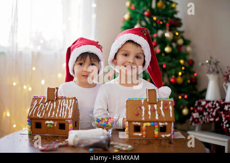 Due ragazzi dolce, fratelli, rendendo gingerbread cookies house, la decorazione a casa nella parte anteriore dell'albero di Natale, bambini che giocano e Foto Stock