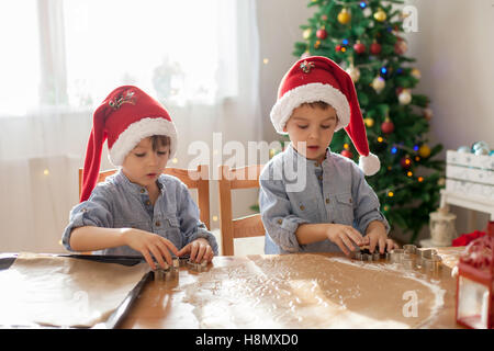 Due simpatici ragazzi con santa hat, preparazione di biscotti a casa, albero di Natale dietro di loro Foto Stock