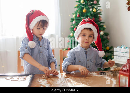 Due simpatici ragazzi con santa hat, preparazione di biscotti a casa, albero di Natale dietro di loro Foto Stock