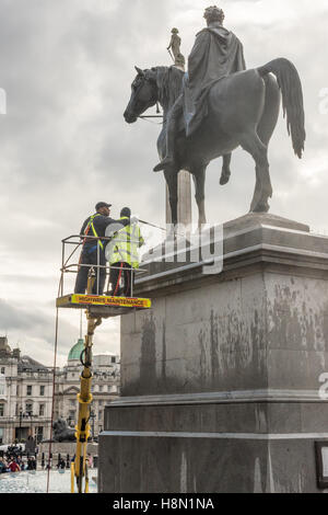 Operai in cima a un cherrypicker la spruzzatura di acqua su di una statua in bronzo di Re Giorgio IV e il suo cavallo in Trafalgar Square, Londra, Regno Unito. Foto Stock