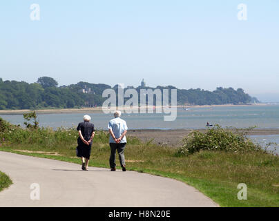 Coppia di anziani a piedi lungo Weston Parade, Weston Shore Woolston, Southampton, Hampshire, Regno Unito con il Royal Victoria Country Park Foto Stock