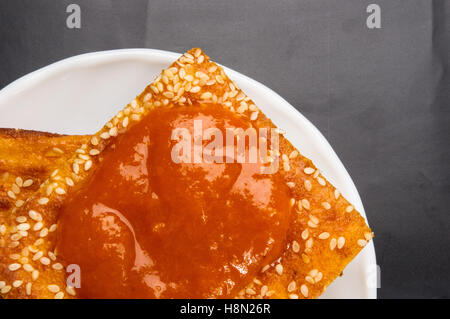 Fetta di cheesecake con semi di sesamo e marmellata di albicocche su sfondo nero Foto Stock