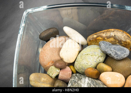 Multicolore ciottoli decorativi in recipienti di vetro su uno sfondo nero Foto Stock