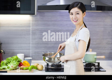 Felice giovane donna cinese per la cottura in cucina Foto Stock
