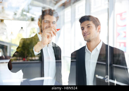 Due felice successo i giovani imprenditori la scrittura sulla scheda di vetro in office Foto Stock