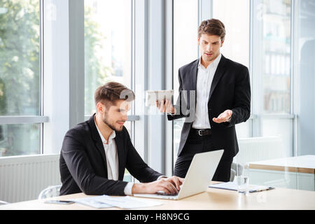 Due graziosi giovani imprenditori e di lavoro utilizzando laptop e tablet in ufficio Foto Stock