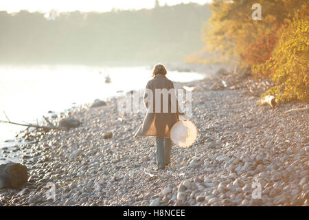 Donna che cammina lungo la costa rocciosa al tramonto Foto Stock